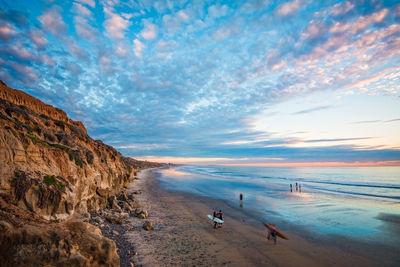 People on beach against sky during sunset