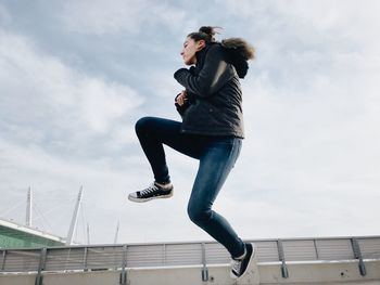 Low angle view of woman jumping against sky