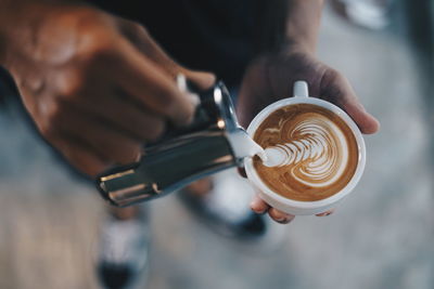 Low section of person pouring milk in cappuccino