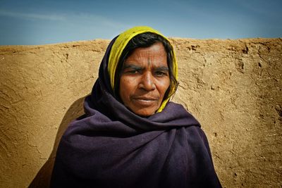 Portrait of old indian woman standing against wall