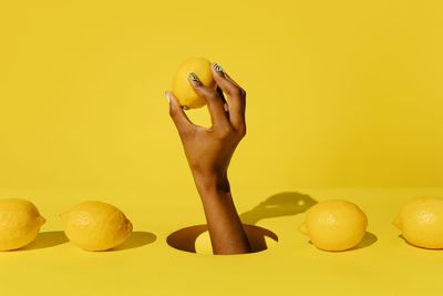 Close-up of hand holding fruit against yellow background