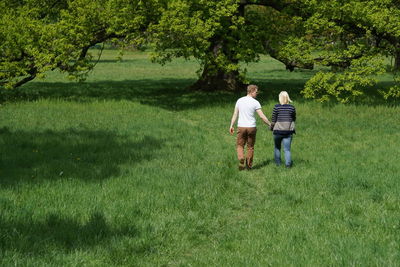 Rear view of couple walking on grassy field in park