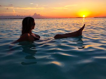 Full length of woman in sea against sky during sunset