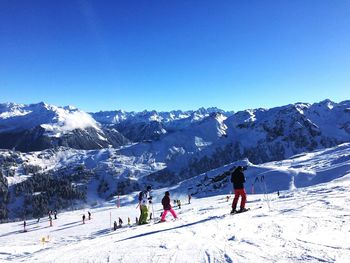 People skiing on snowcapped mountains against clear blue sky