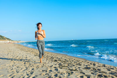 Young woman running at beach against clear blue sky
