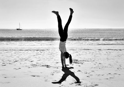 Full length of girl doing handstand at beach against sky