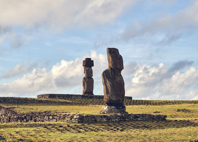 Stack of moai statues on field against sky