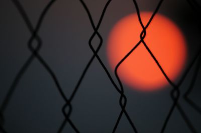 Close-up of chainlink fence against sky during sunset