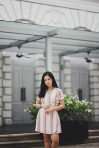 Portrait of young woman standing against building