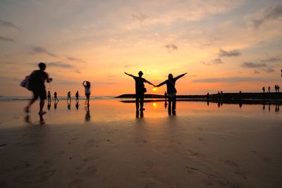 Silhouette people at beach against sky during sunset