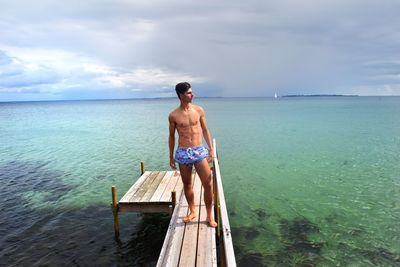 Full length of shirtless man standing on pier over sea against sky