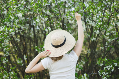 Young beautiful woman in a hat among flowering trees. back view