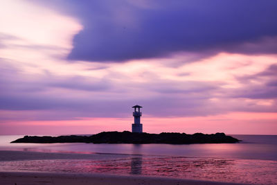 Lighthouse by sea against sky during sunset