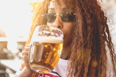 Close-up of woman wearing sunglasses drinking beer