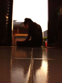 Side view of woman sitting on tiled floor at home