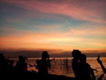 Silhouette people on beach against sky during sunset