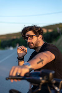 Fashionable young man sitting and smoking on a classic motorbike in sunset.