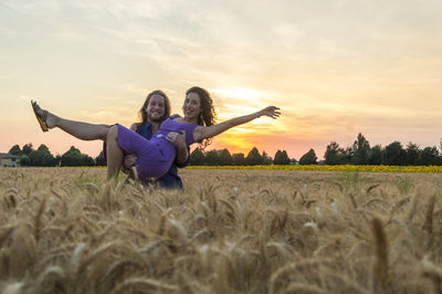 Woman smiling on field against sky during sunset