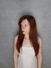 Woman looking away while standing against wall