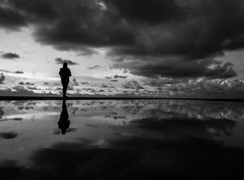 Silhouette man standing in water against sky