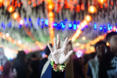 Close-up of woman showing stop sign while standing in illuminated market at night