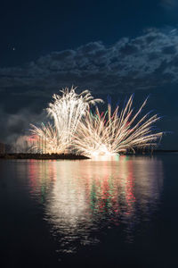 Firework display over lake against sky at night