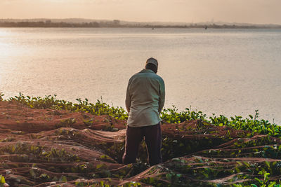 Rear view of man walking at beach against sky during sunset