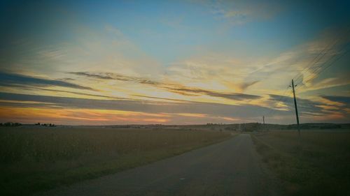 View of country road along landscape at sunset