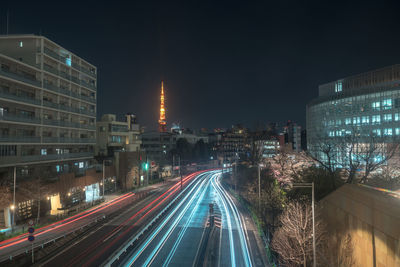Light trails on road amidst buildings against sky at night