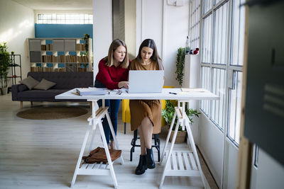 Businesswoman leaning by colleague using laptop at desk in office