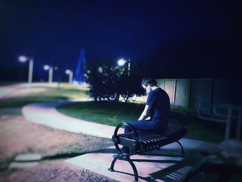 Side view of young man sitting on bench in park