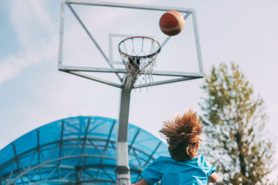 Rear view of woman with basketball hoop against sky