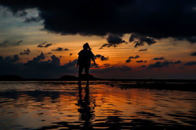 Silhouette man standing in sea against sky during sunset