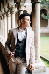 Young man looking away while standing against built structure