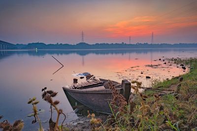 Fishing boat moored in lake against sky during sunset