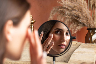 Mirror reflection of woman applying under-eye patch at dressing table closeup