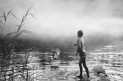Rear view of boys standing on lake against sky