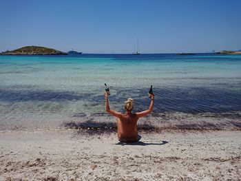 Rear view of shirtless man standing at beach against clear sky