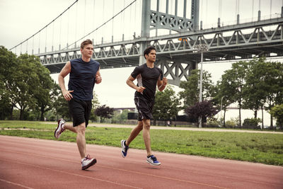 Friends running on sports track against triborough bridge