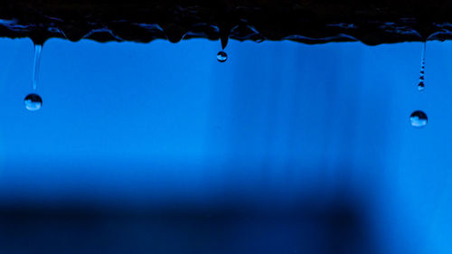 Low angle view of water drops falling against blue sky