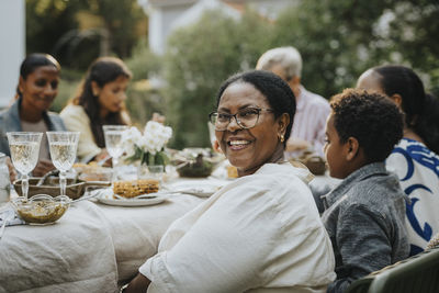 Portrait of happy senior woman with eyeglasses looking over shoulder while sitting with family members at lunch