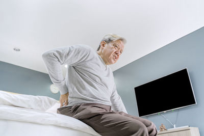 Low angle view of senior man with backache sitting on bed at home