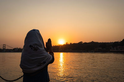 Young indian girl praying the holy ganges river and sun setting at horizon at river bank