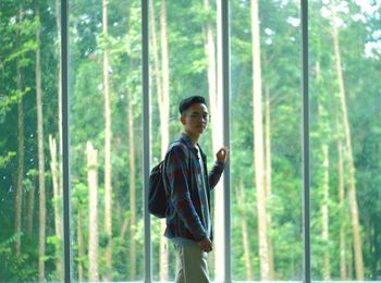 Portrait of young man standing by window in forest