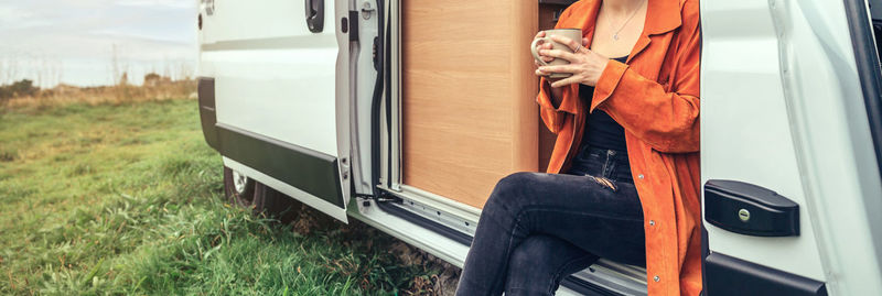 Midsection of woman holding cup sitting in motor home