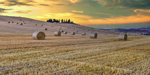 Hay bales on field against sky during sunset