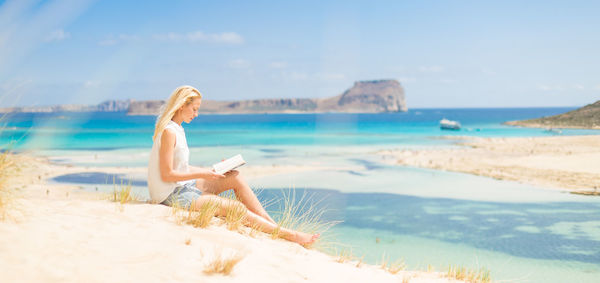 Woman relaxing on beach against sky