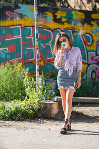Beautiful woman holding compact disc while standing against graffiti wall