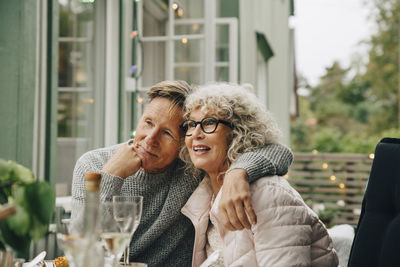 Thoughtful senior man sitting with arm around woman at dining table during garden party