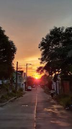 Road amidst trees and buildings against sky during sunset